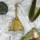 Brass bell, green feathers, a shamanic themed oracle card, and stone on white fabric