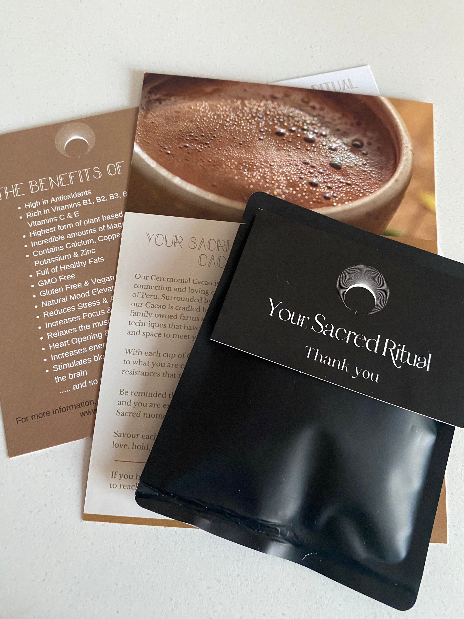 A black sample bag of Cacao with pieces of raw cacao and some 'Sacred Ritual' branded card stock.