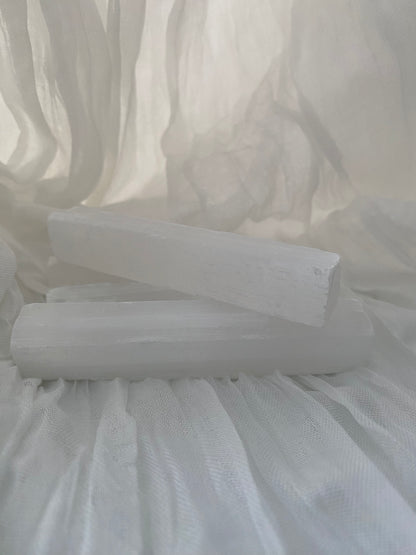 Raw Selenite Sticks placed on a white, light filtering  fabric.