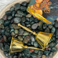 Two brass bells on a bed of small moss agate stones with a tarot card featuring an Air Guardian.