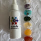 A spray bottle labeled 'Samadhi - Chakra Balancing Mist' with a white label, alongside a collection of colorful gemstones corresponding to the chakras, displayed on a white textured surface.