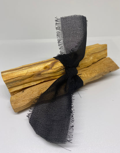 Three palo santo sticks wrapped in a black see through ribbon on a white background.