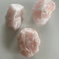 Three rose quartz chunks on a white stone surface from top view.