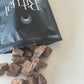 Cacao pieces spilling out of a white bag, laying flat labeled 'Sacred Ritual' on a benchtop.