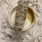 A bundle of Californian White Sage laying flat  on white fabric with scattered howlite stones.