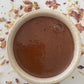 Warm cup of Cacao in a ceramic cup on a surface with pink and yellow dried flowers and some gold leaf.