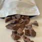 Cacao pieces spilling out of a white bag, laying flat labeled 'Sacred Ritual' on a benchtop.