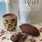 Ceremonial Grade Cacao in a leopard print cup and 'Sacred Ritual' packaging on a light surface with pieces of cacao and a dried cacao pod in front.