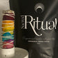 Black 'Sacred Ritual' bag of cacao with a colorful smudge stick and white container on a gray surface.