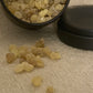 Frankincense Incense resin in a black tin on a textured beige surface shown as a close up shot.