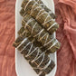 Multiple mugwort bundles tied and displayed on a white textured platter sitting on rose coloured fabric.