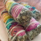 Colourful rose petals tied to Californian White sage bundle to represent each colour of the chakras  on a white plate. Side View.
