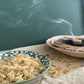 Small bowl of resinous, loose frankincense in front of a smoke coming from burning frankincense on a charcoal disc in the background.
