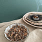 Two ceramic containers with resin, one is a bowl, the other is a shell with burning myrrh on a charcoal disc and smoke with  a textured green background. 