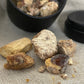 Close up shot of Dark Copal resin with a small black packaged tin in the background on beige linen.