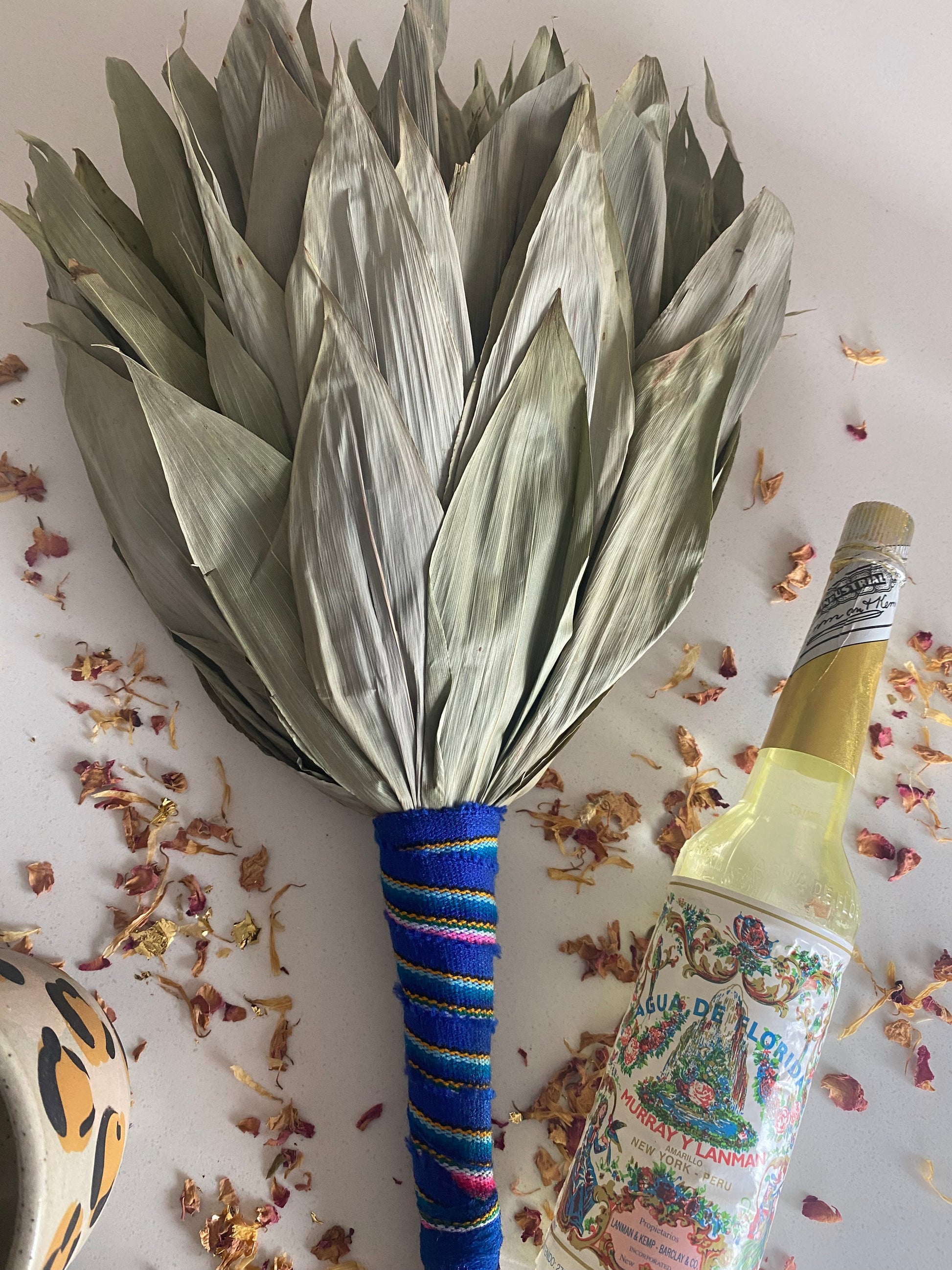 Dried leaf rattle tied with a vibrant Peruvian ribbon on a white surface with dried flowers scattered around