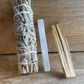 A smudge kit consisting of a white sage stick, a palo santo stick, and a selenite crystal stick, all arranged on a wooden surface.